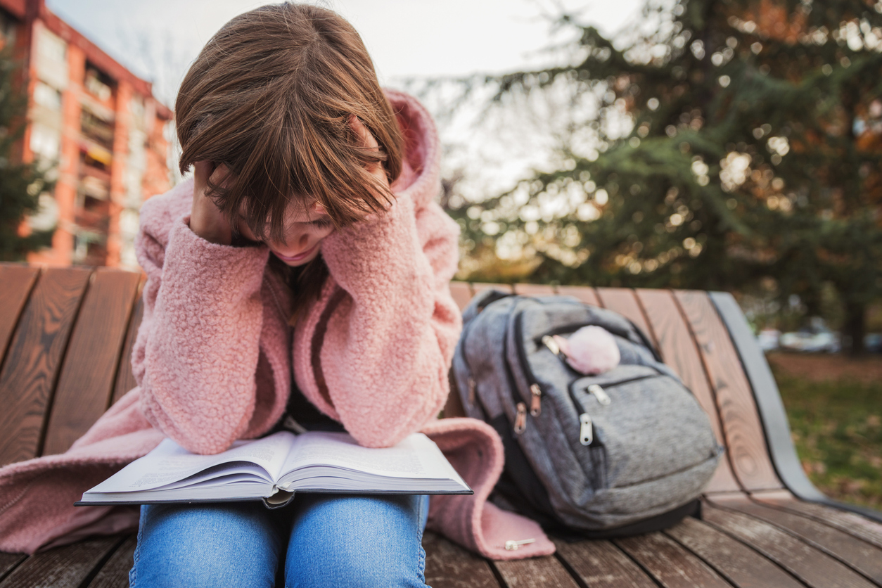 Nervous teenage girl with head in her hands reading in the park